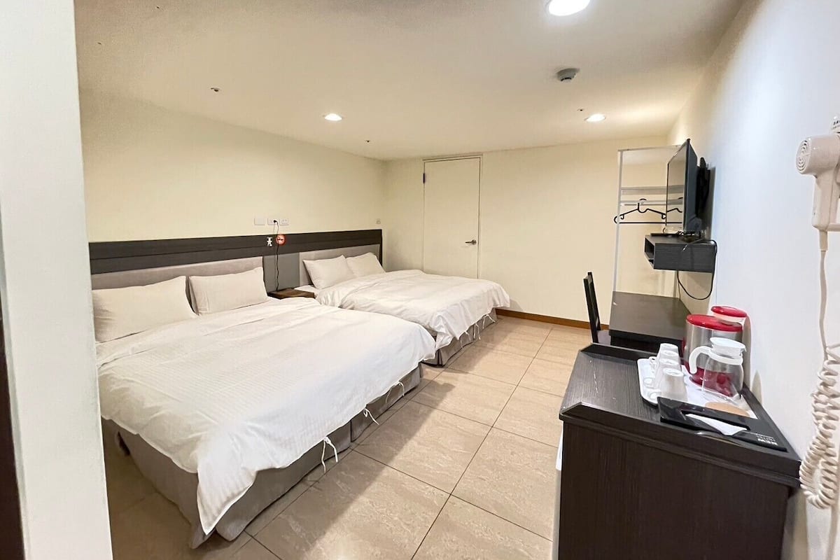 A hotel room with two beds, a desk with a mirror, a hairdryer, and a TV.