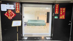 Entrada de hotel com uma cama verde no quarto, um letreiro na porta e decorações chinesas.