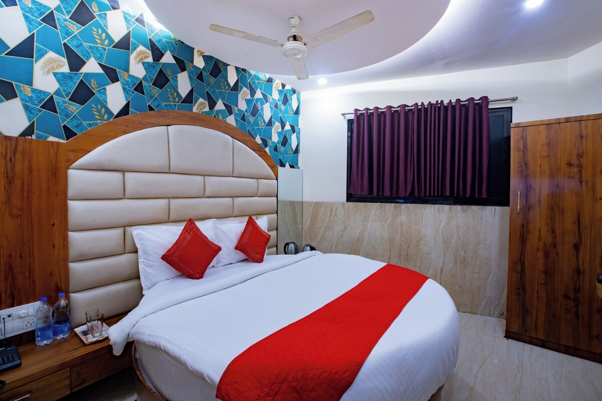 Habitación de hotel con cama, ventilador de techo, televisor y ventana con cortinas.