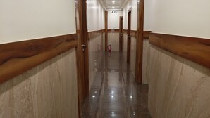 Un couloir aux murs lambrissés et au sol en marbre, qui mène à plusieurs portes.