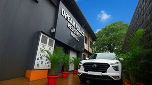 Un VUS blanc est garé devant un bâtiment portant l’inscription « Dream Palace Residency Hotel », avec des plantes en pot et un ciel bleu clair en arrière-plan.