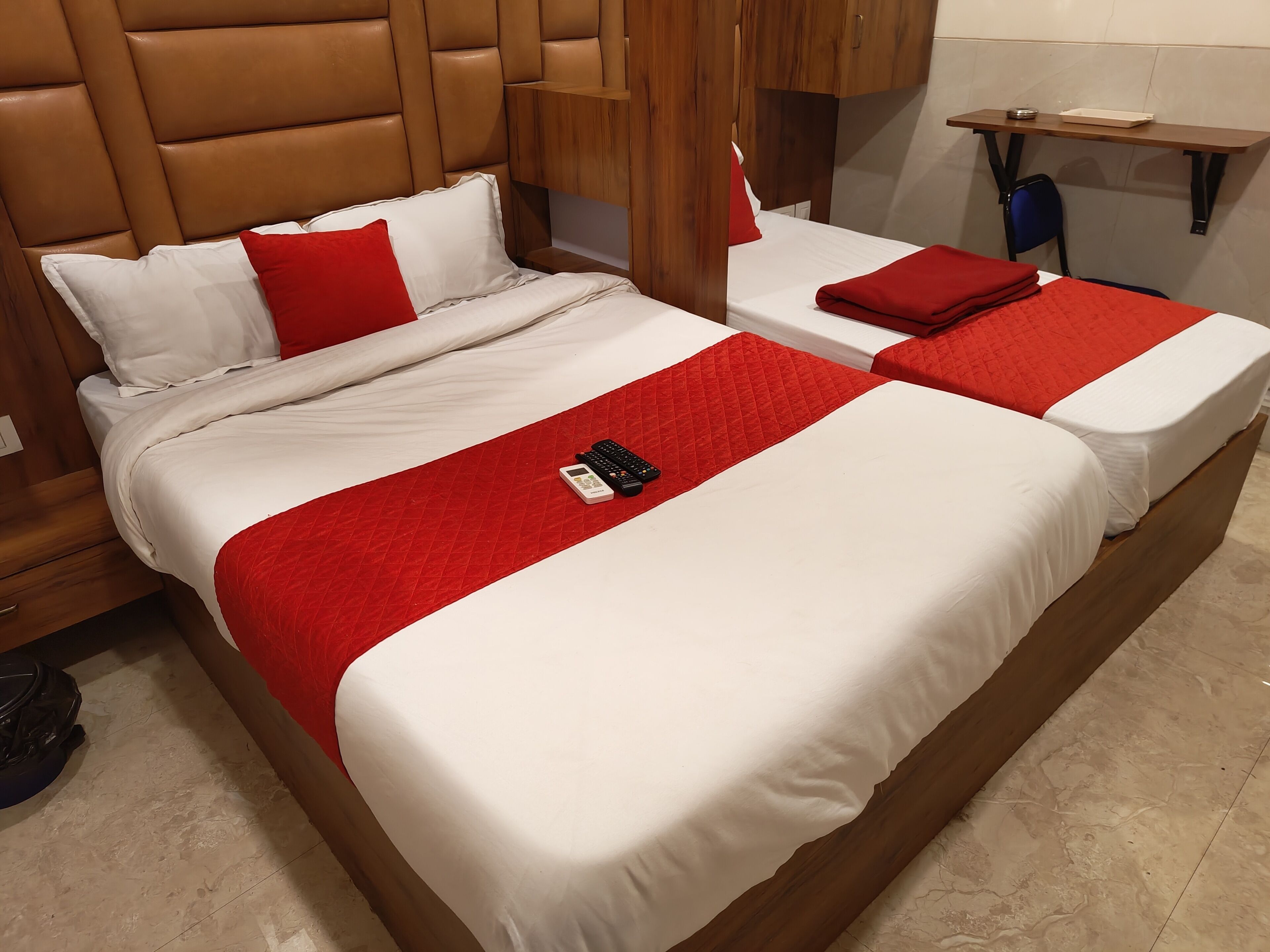 Un lit double avec une couvre-lit rouge matelassée, un oreiller blanc et une télécommande posés sur le lit.
