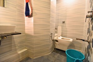 Une salle de bain avec des toilettes blanches, un lavabo et un seau bleu.