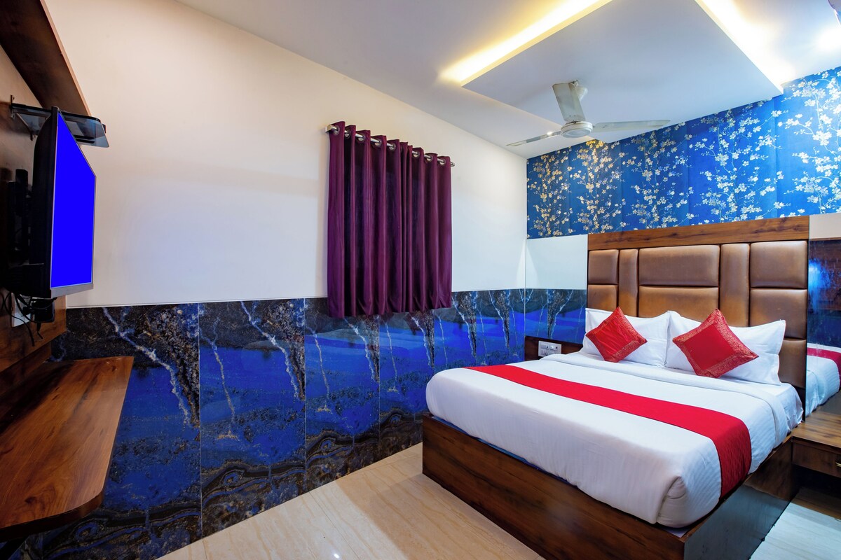 Una habitación de hotel con una cama, cabecera de madera, pared con diseño de mármol, ventilador de techo y televisión.
