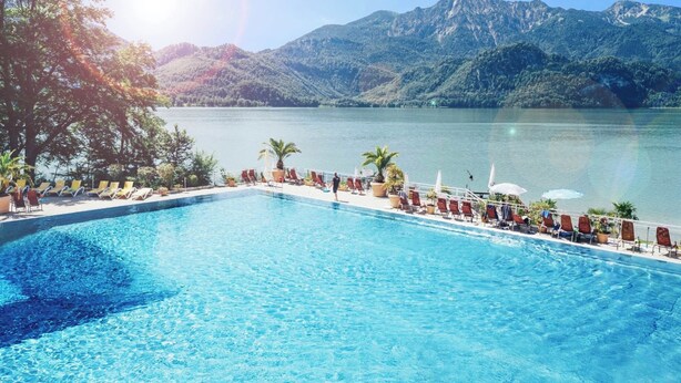 A pool with clear blue water, surrounded by lounge chairs and potted plants, overlooking a lake with mountains in the background. - Spacious, cozy attic apartment with mountain views on 1.5 floors (Berg)