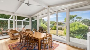 A spacious dining area with a large table and chairs, large windows, and a view of a lush garden. - Callaway House - Point Lonsdale (Point Lonsdale)