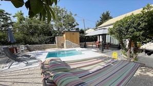 Un patio trasero con piscina, sillas de descanso, una hamaca y una pequeña construcción de madera.