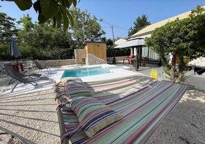 Quintal com piscina, cadeiras de descanso, rede e uma pequena construção de madeira.