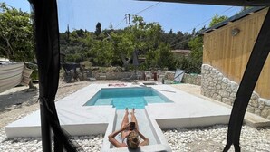 Una persona descansando junto a una piscina con vistas a un jardín y un edificio de madera.