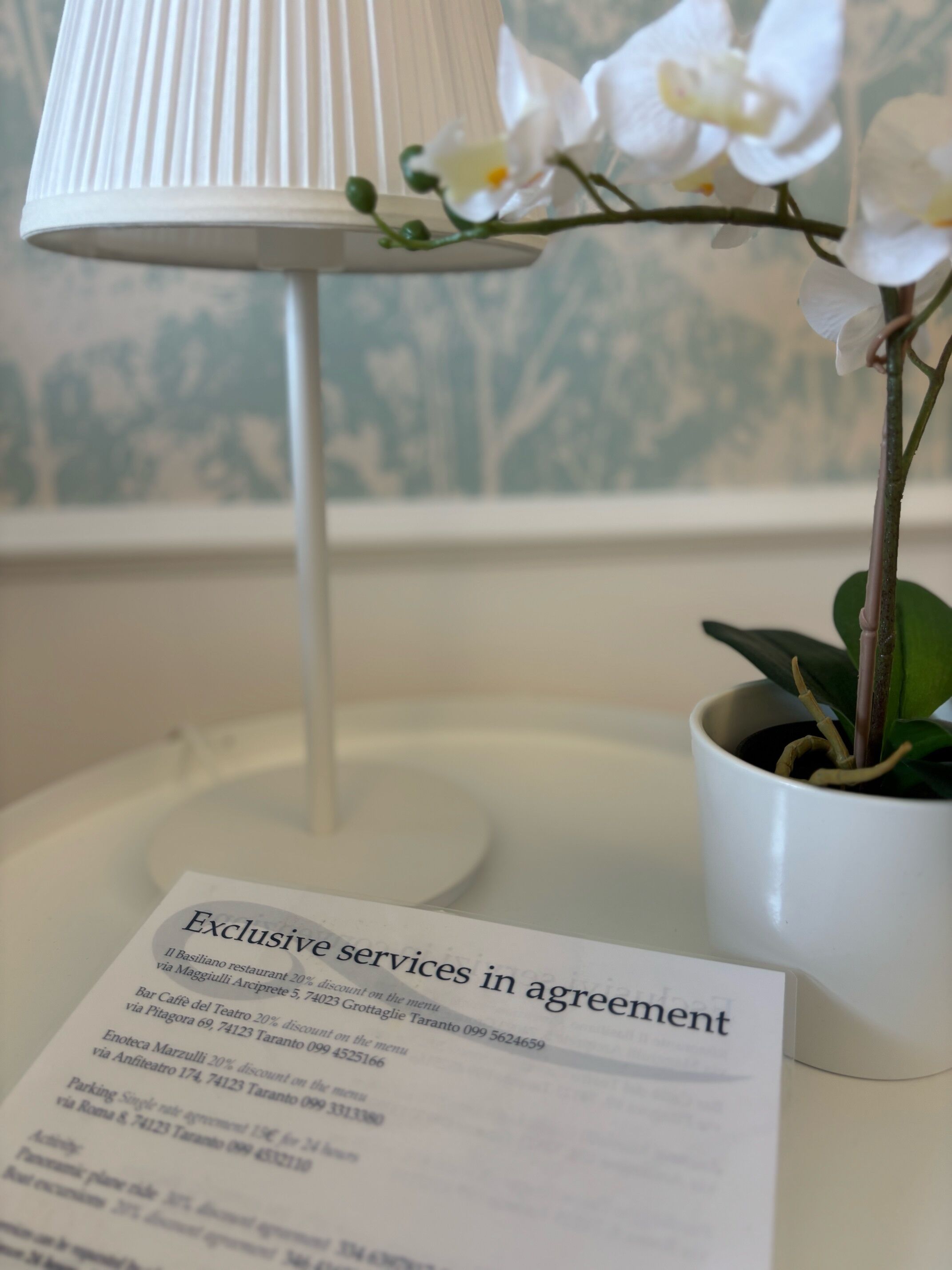 Et hvidt bord med en orkidé i potte og en lampe, samt en menu med restauranttilbud.