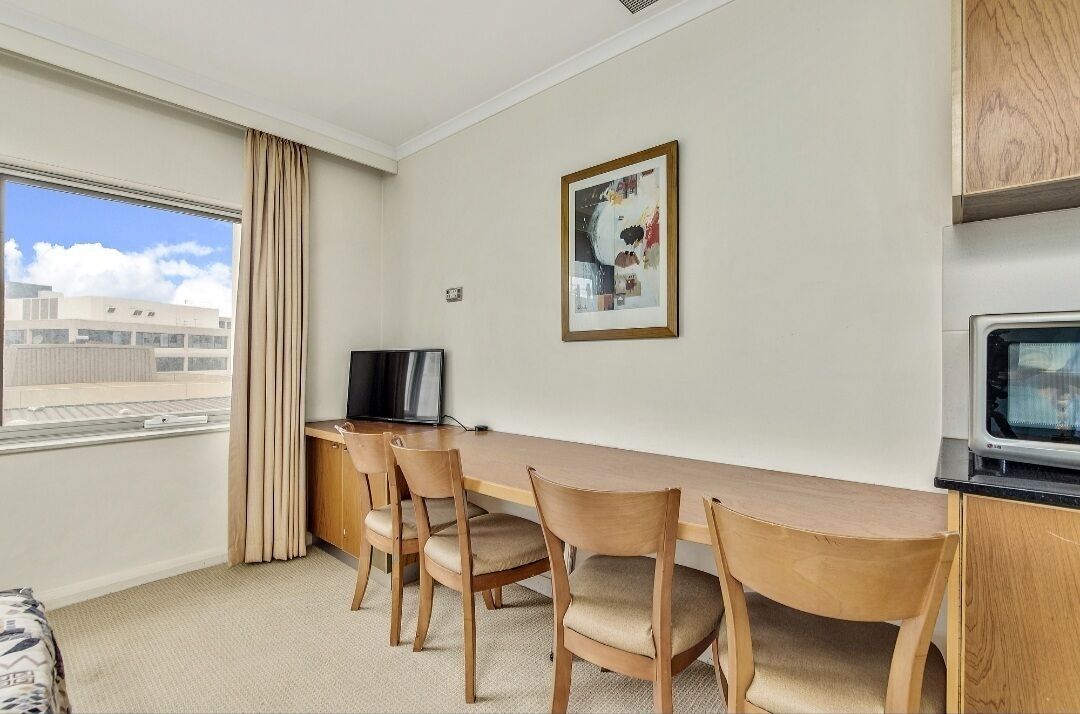 A hotel room with a wooden desk, chairs, a television, a framed picture on the wall, and a window with curtains.