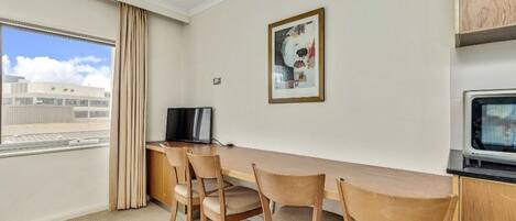 A hotel room with a wooden desk, chairs, a television, a framed picture on the wall, and a window with curtains.