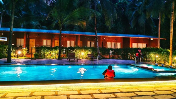 Une piscine où une personne porte un gilet de sauvetage rouge, entourée de palmiers et d’un bâtiment doté de nombreuses fenêtres.