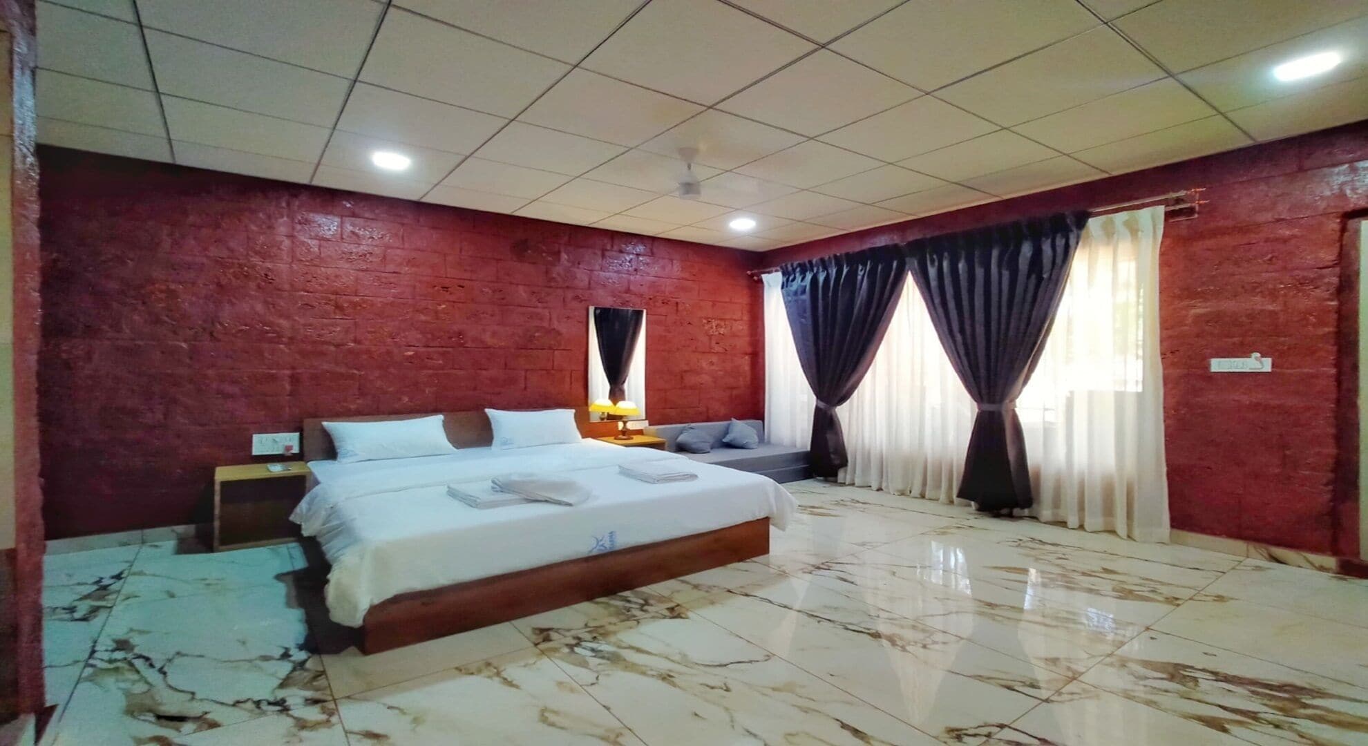Une chambre d’hôtel avec un grand lit, une table de chevet, une lampe et une fenêtre avec des rideaux.