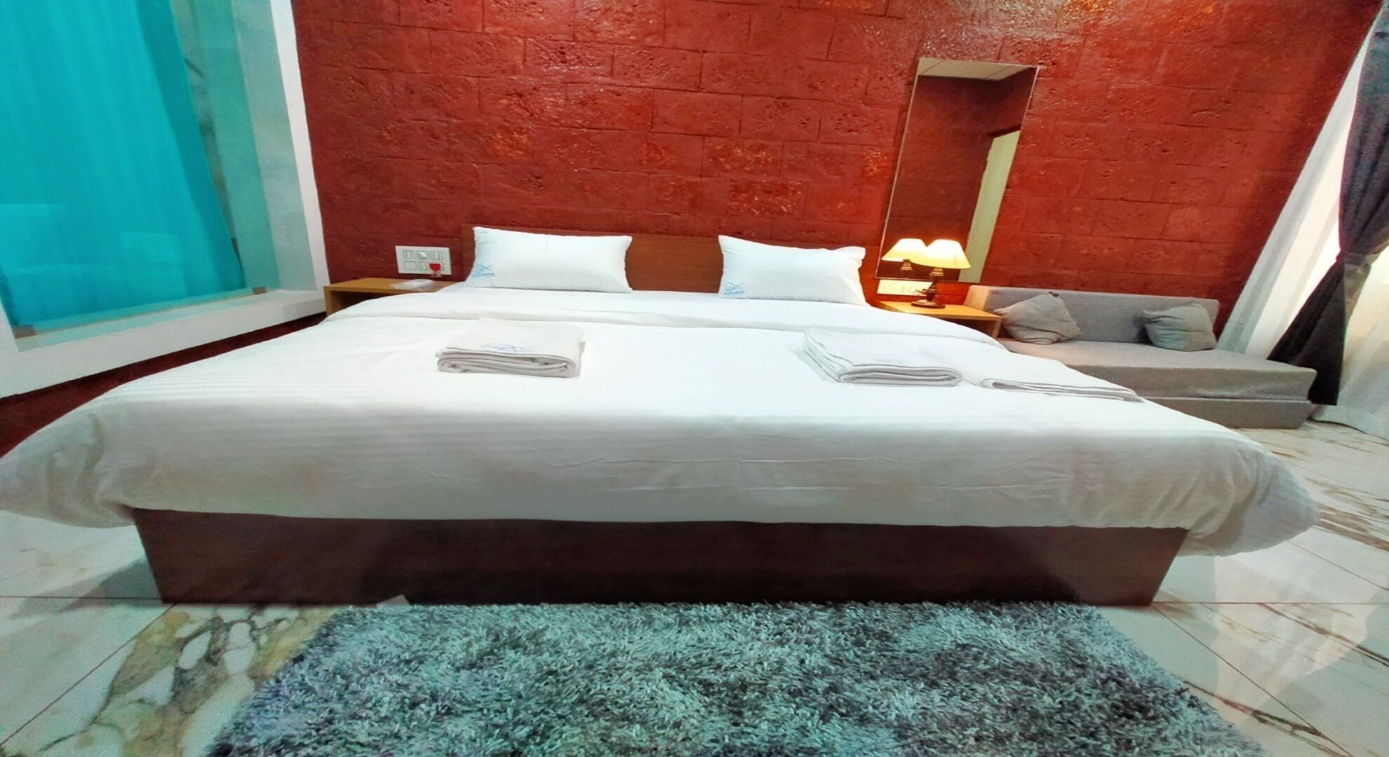 Una camera d'albergo con un letto grande, un comodino, una lampada, un divano e uno specchio.