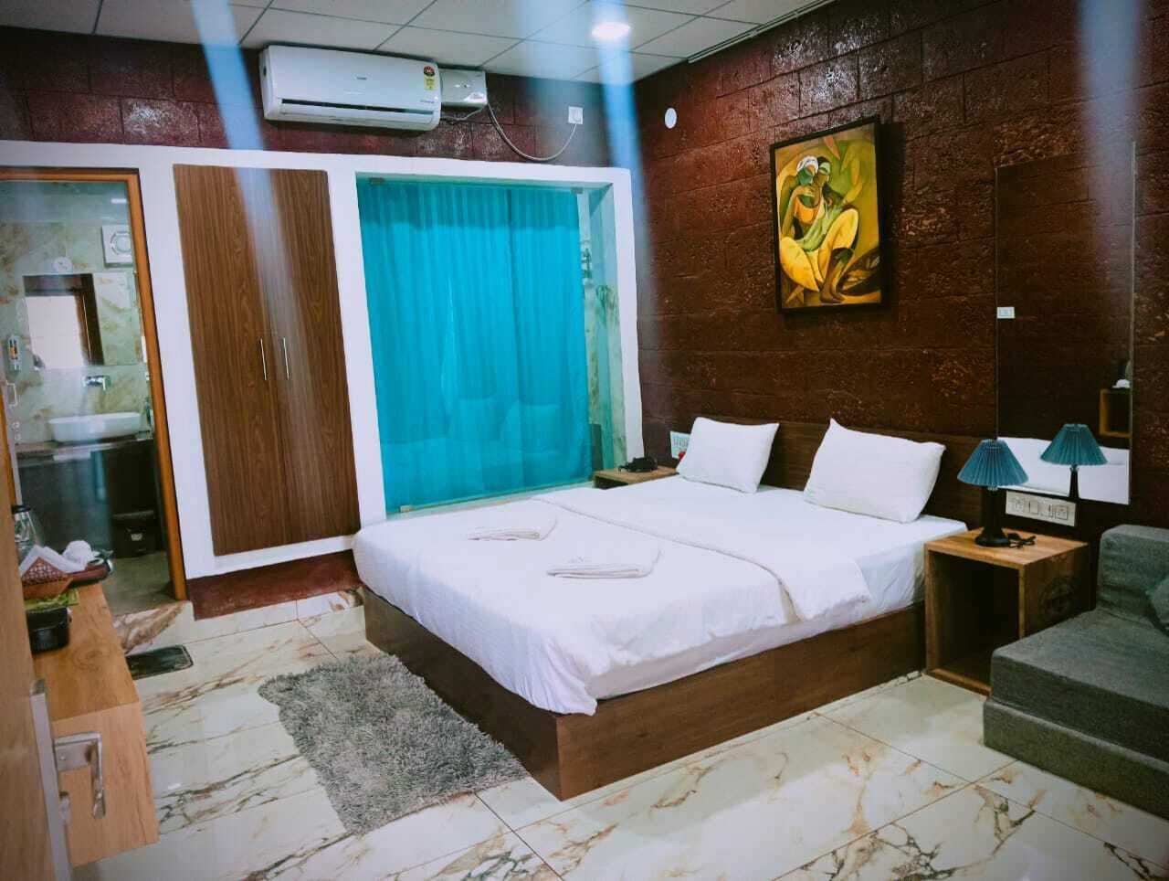 Un dormitorio con cama, mesita de noche, lámpara, sofá, puerta corrediza y un cuadro en la pared.