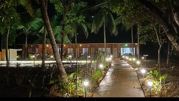 A pathway leading to a building with multiple windows, surrounded by trees and illuminated by street lamps.