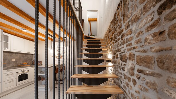 A modern staircase with wooden steps and black risers, leading to a kitchen area with white cabinets and a stone wall. - Modern apartment for 2 persons in the Porec old town , only 150m from the beach. (Porec)