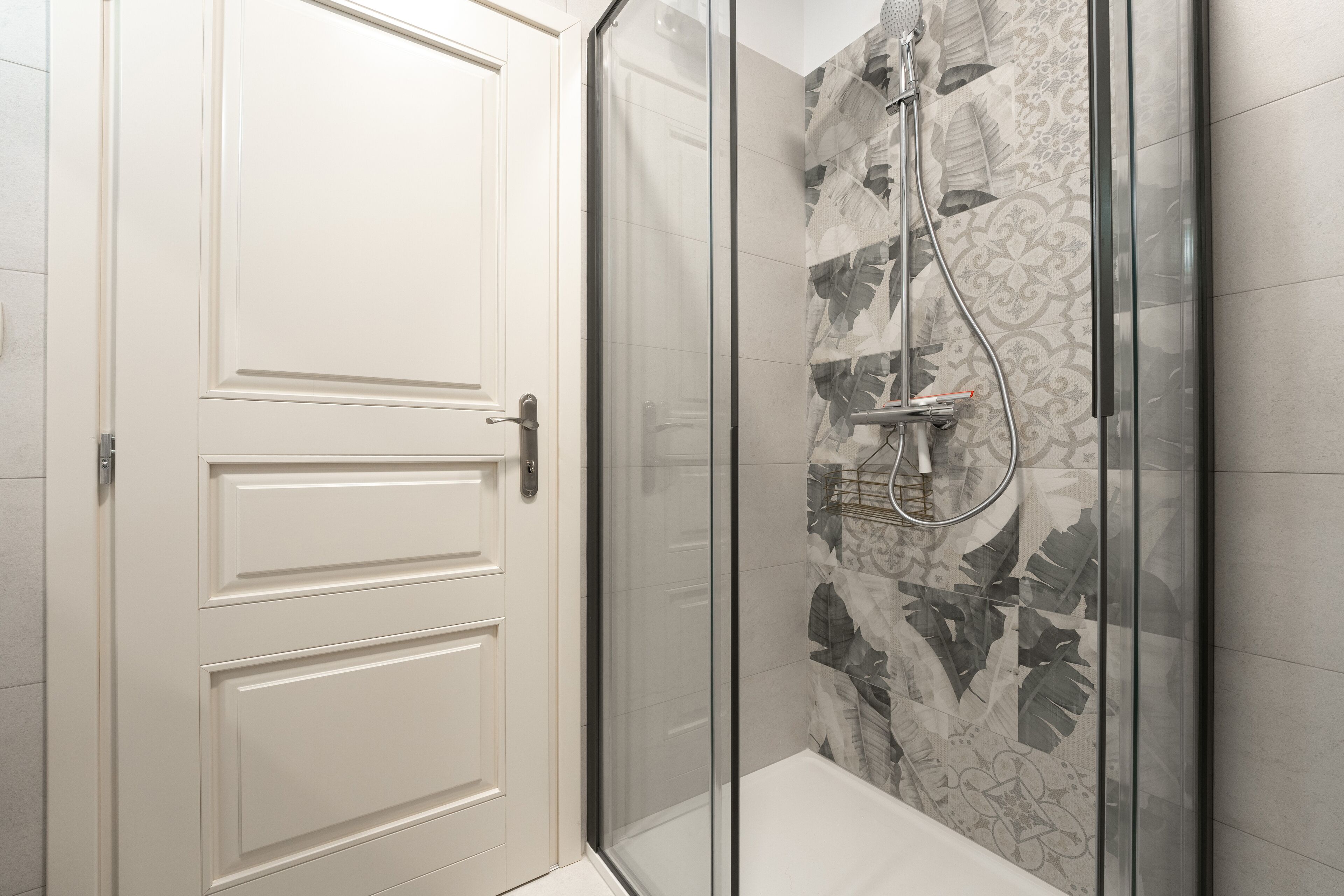 Une salle de bain moderne avec une douche à parois de verre, une porte blanche et des carreaux à motifs.