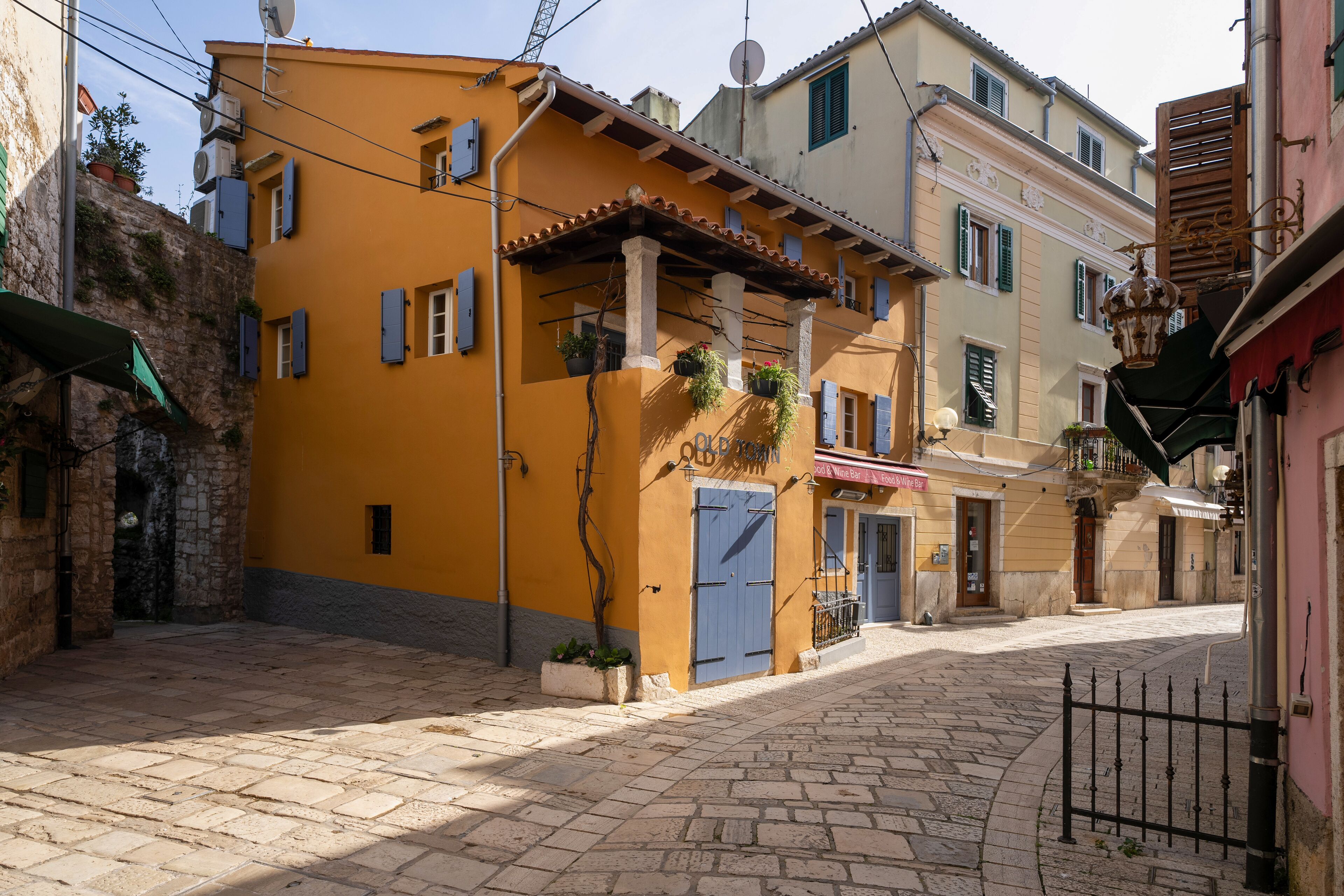 A narrow cobblestone street with buildings featuring balconies and potted plants.