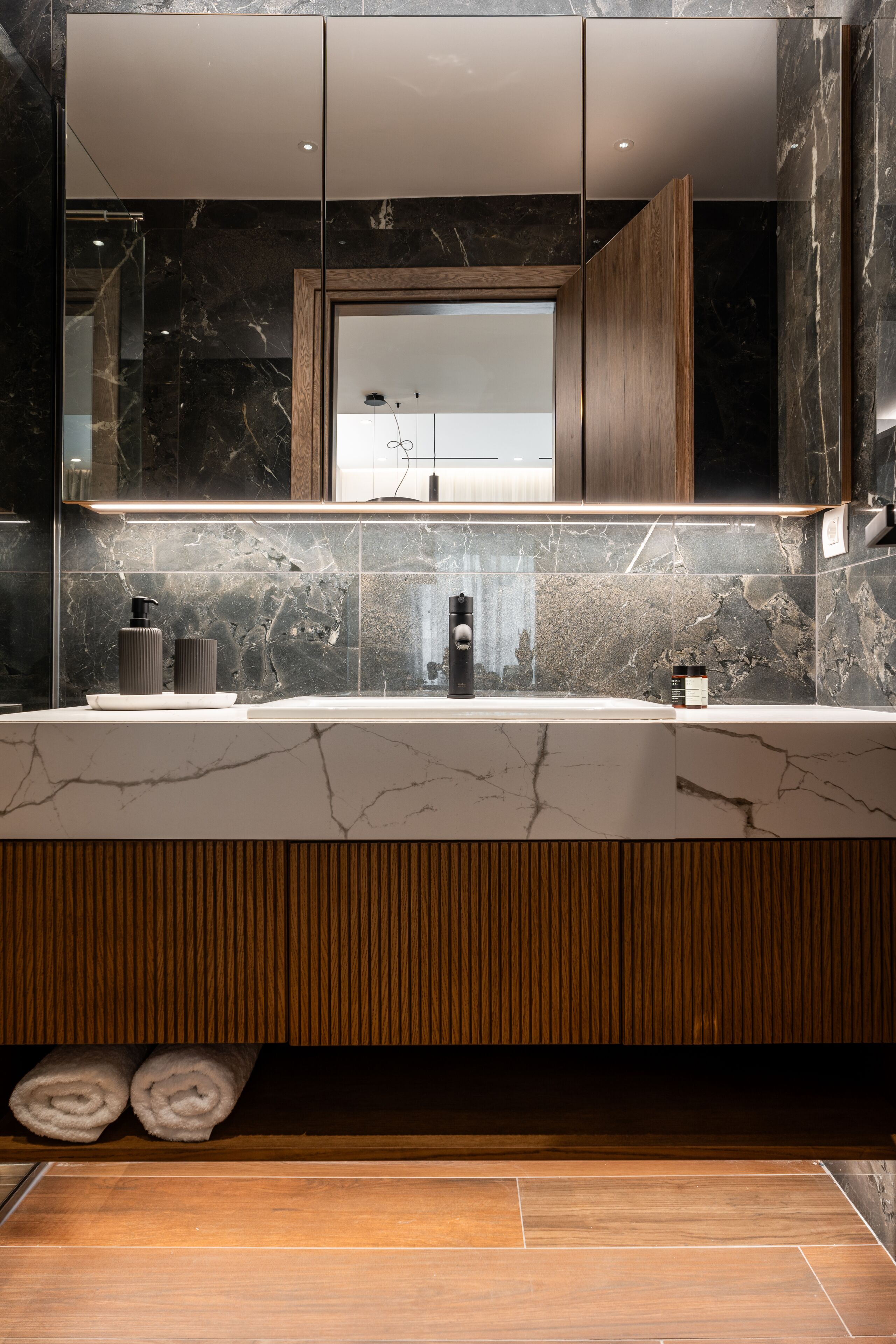 A modern bathroom with a marble sink, wooden vanity, and a large mirror.