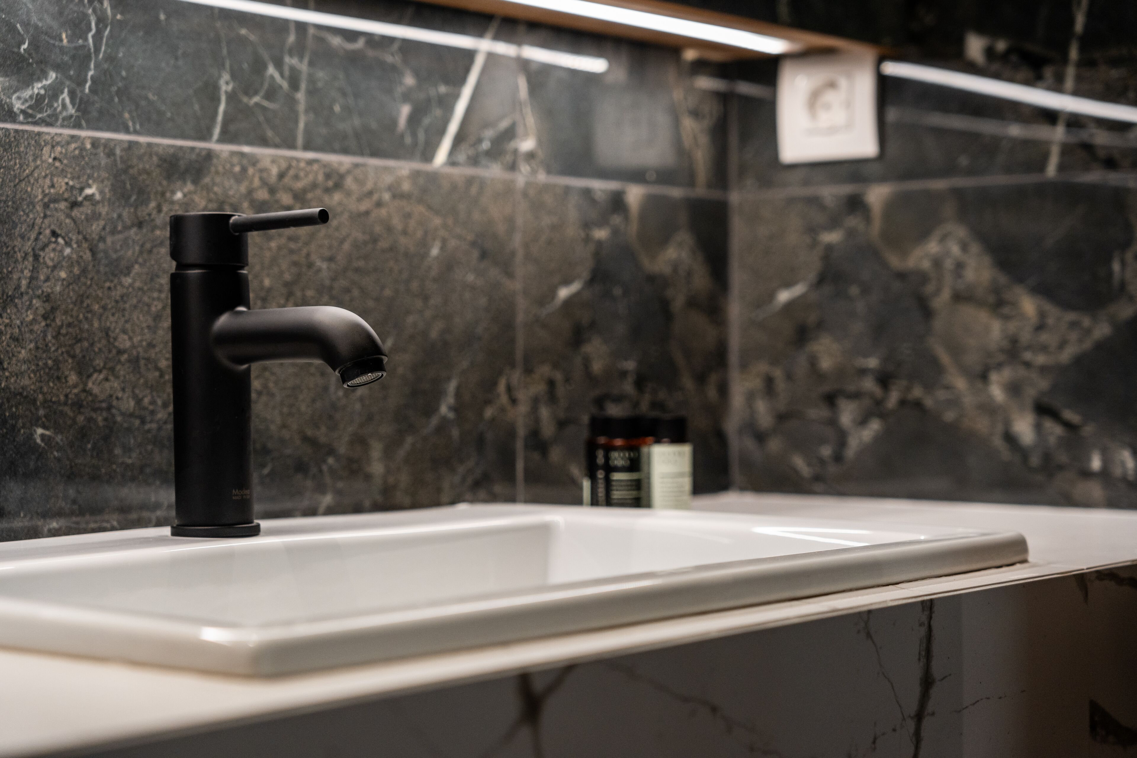 A modern bathroom with a black faucet, white sink, and dark marble walls.