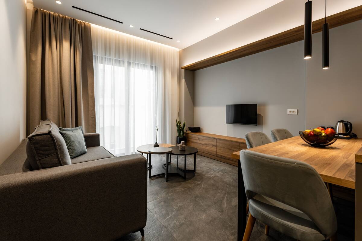 Een moderne woonkamer met een bank, een eettafel en een aan de muur bevestigde televisie.