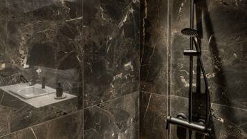 Un baño moderno con ducha de vidrio, paredes de mármol y zona de lavamanos visible.