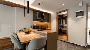 A modern kitchen with a wooden dining table, grey upholstered chairs, and pendant lighting.