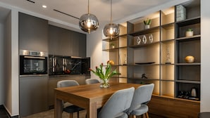 A modern kitchen with a wooden dining table, grey chairs, and a glass vase with flowers.