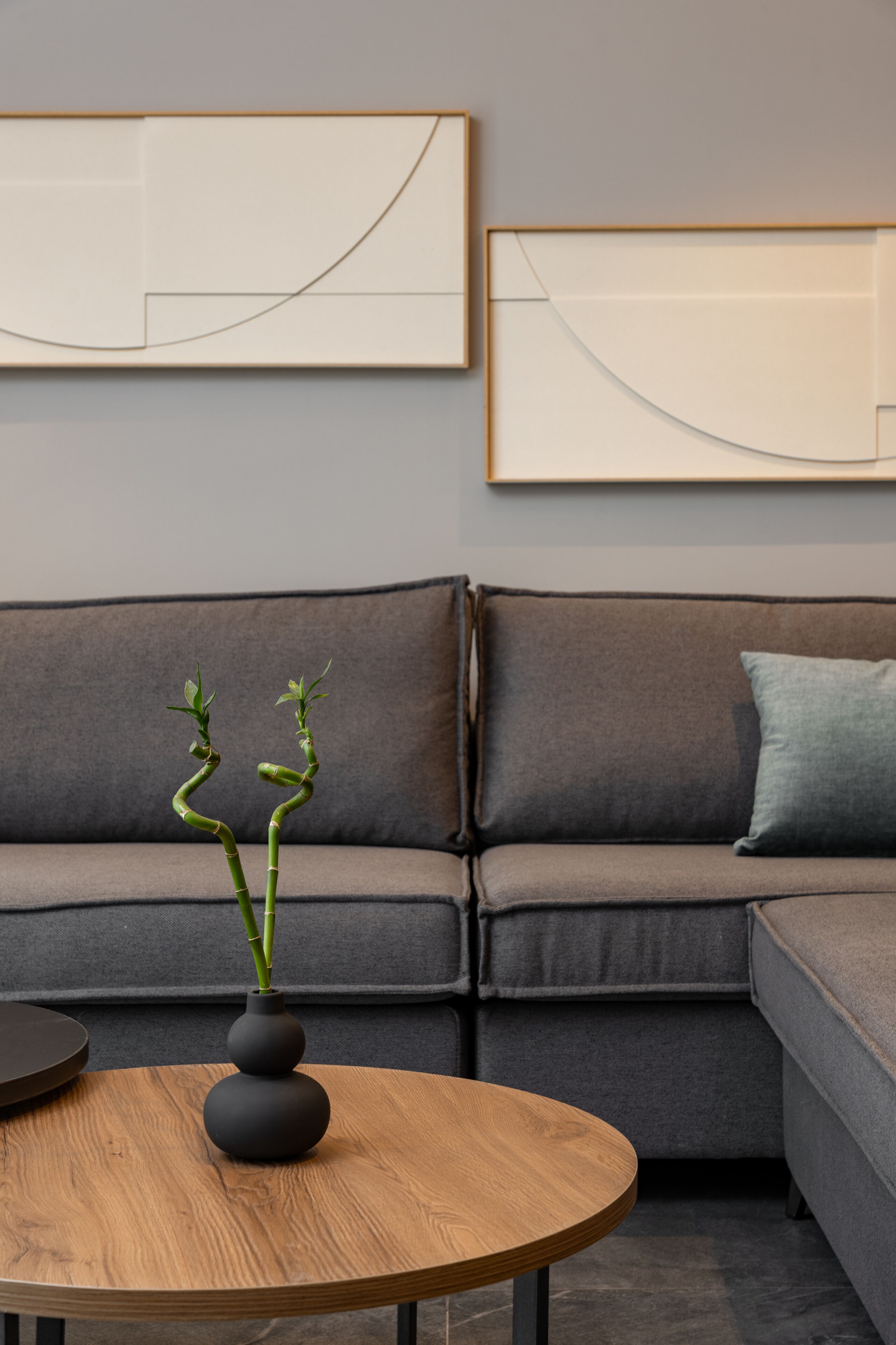 En moderne stue med et rundt træbord, en mørkegrå sofa og et minimalistisk kunstværk over sofaen.