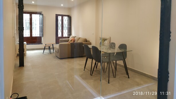 Amplia sala de estar con mesa de comedor de vidrio, un sofá y un ventanal grande.