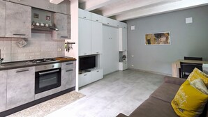 A modern kitchen with built-in appliances, a dining area with a table and chairs, and a living space with a sofa and cushions. - Perla House (Ferentillo)
