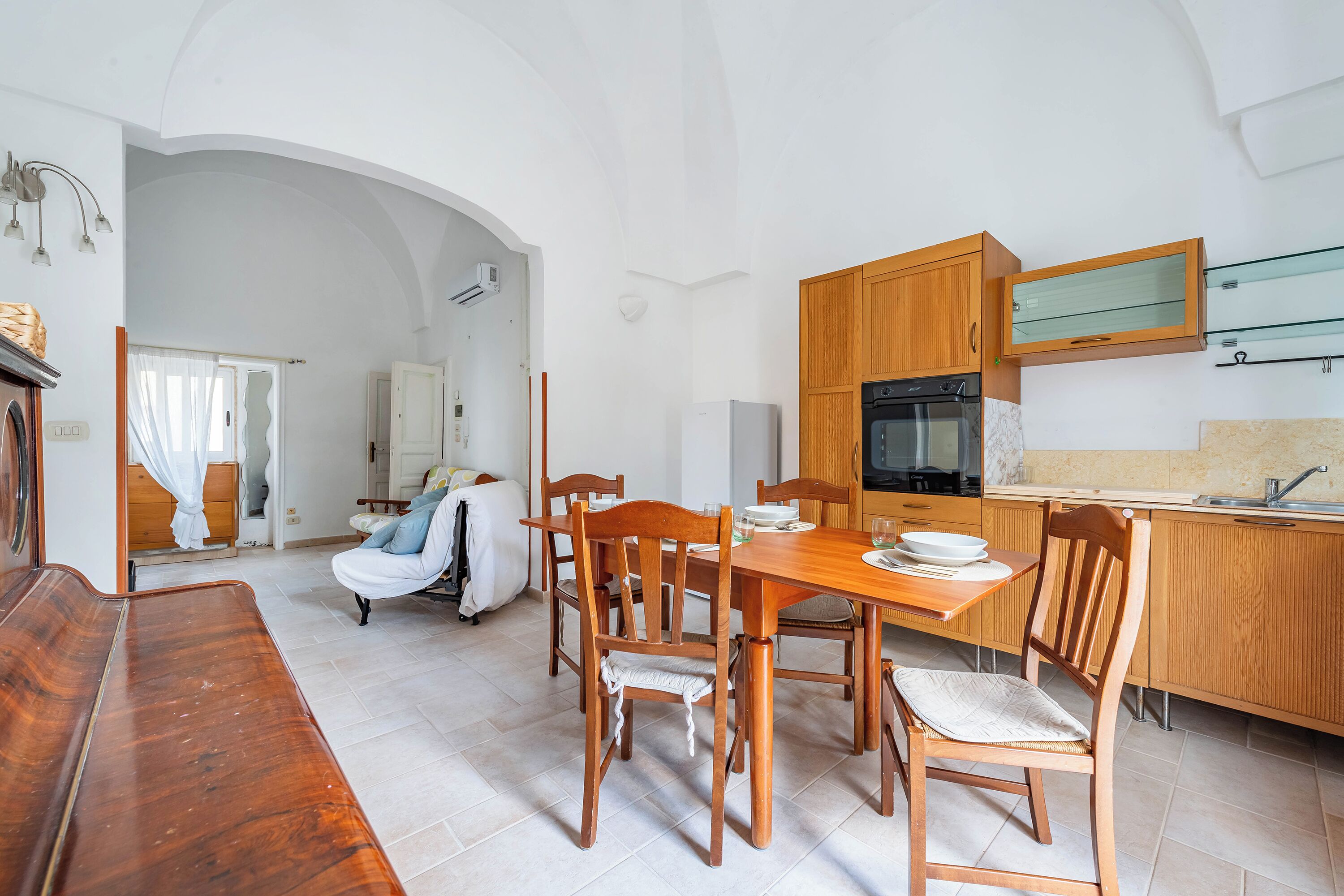 Un vaste espace de vie comprenant une table et des chaises de salle à manger en bois, un canapé et une cuisine dotée de meubles en bois et d’un four encastré.