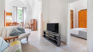 A living room with a sofa, TV, and a dining area in the background. - Pianista Home in Fasano City (Fasano)