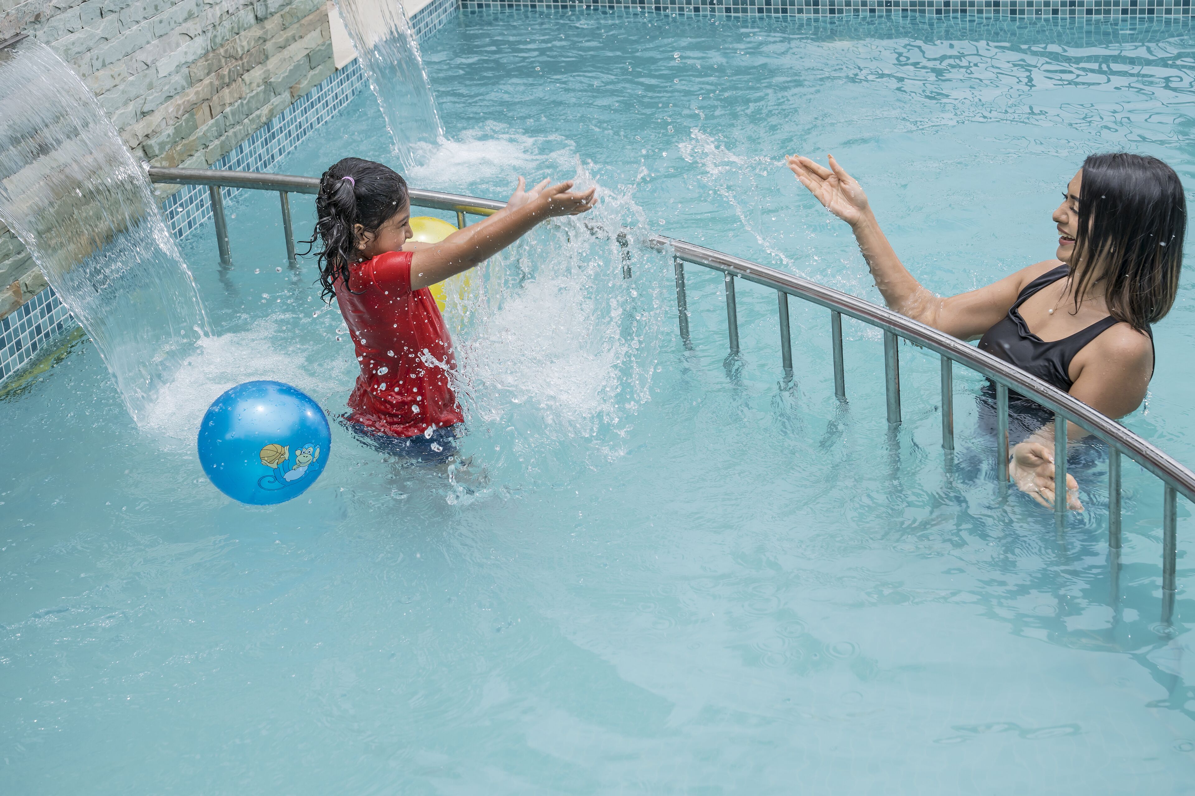 A swimming pool with clear water, a metal railing, and a blue ball.