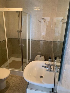 A bathroom with a glass-enclosed shower, a white sink, and a toilet.