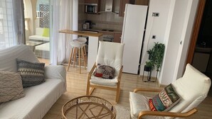 Ein modernes Wohnzimmer mit einer Couch, Sesseln, einem Korbstuhl und einer Küche im Hintergrund.