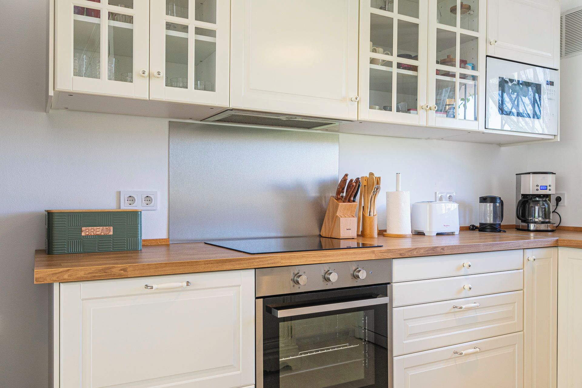 A kitchen with white cabinets, a wooden countertop, a built-in oven, and various kitchen appliances.