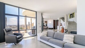 Un vaste espace de vie doté d’une grande fenêtre, d’un canapé gris, d’un fauteuil noir et d’un escalier menant à l’étage supérieur.