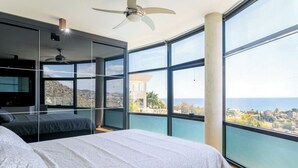 Une chambre avec un grand lit, un ventilateur de plafond et une vue sur la mer.