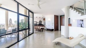 Un vaste espace de vie doté d’un grand mur de verre, d’un coin repas, d’un salon avec un fauteuil inclinable et d’un escalier.