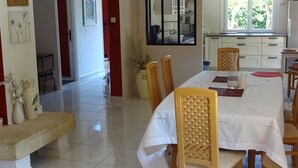 A dining area with a long table, chairs, and a view of the kitchen through a glass door. - Spacious villa in theAude close to the sea, mountains, history and vineyards! (Montazels)