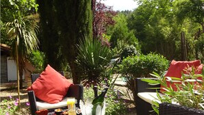 An outdoor seating area with wicker furniture, a table set with a glass of orange juice, a bottle, and a glass of white wine. - Spacious villa in theAude close to the sea, mountains, history and vineyards! (Montazels)