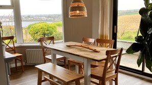 A dining area with a wooden table and chairs, a hanging light fixture, and a view of a river and fields. - Ballydorn Lodge Strangford Lough (Killinchy)