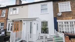 A two-story residential building with a white facade, a front door, and a small garden area.