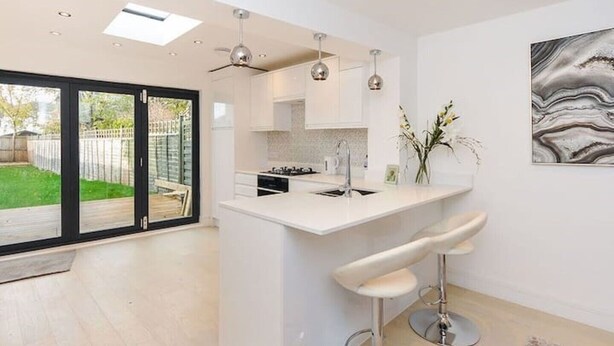 A modern kitchen with a central island, bar stools, pendant lighting, and a view of a backyard through glass doors.