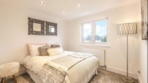 A bedroom with a bed, a window, a radiator, and a floor lamp.