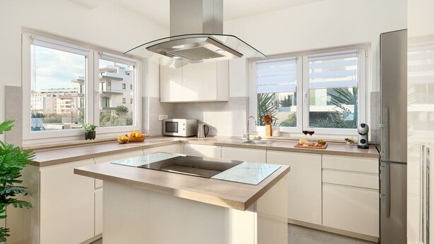 A modern kitchen with a central island, white cabinetry, a stainless steel refrigerator, and large windows offering views of the city. - Sun Spalato Flower (Split)