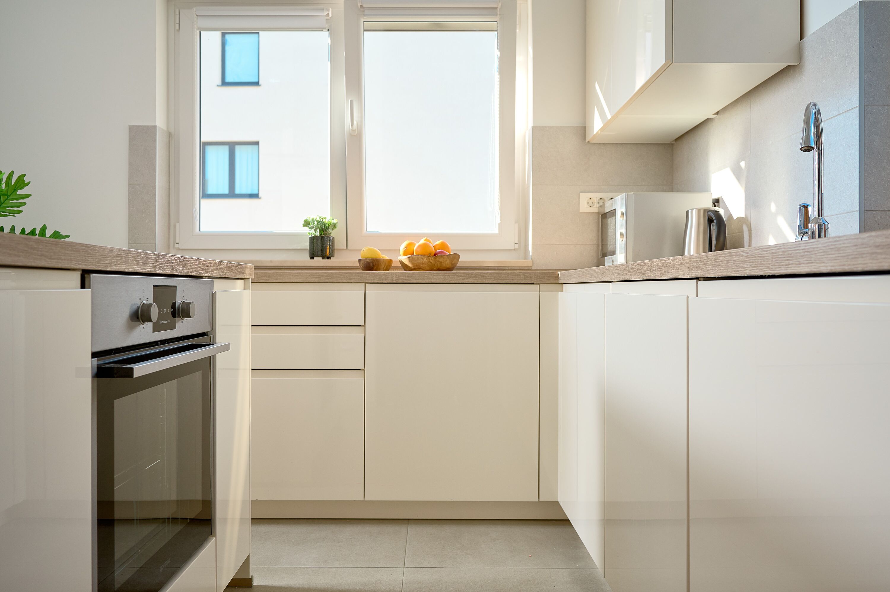 Una cocina moderna con armarios blancos, horno empotrado, microondas y hervidor sobre la encimera.